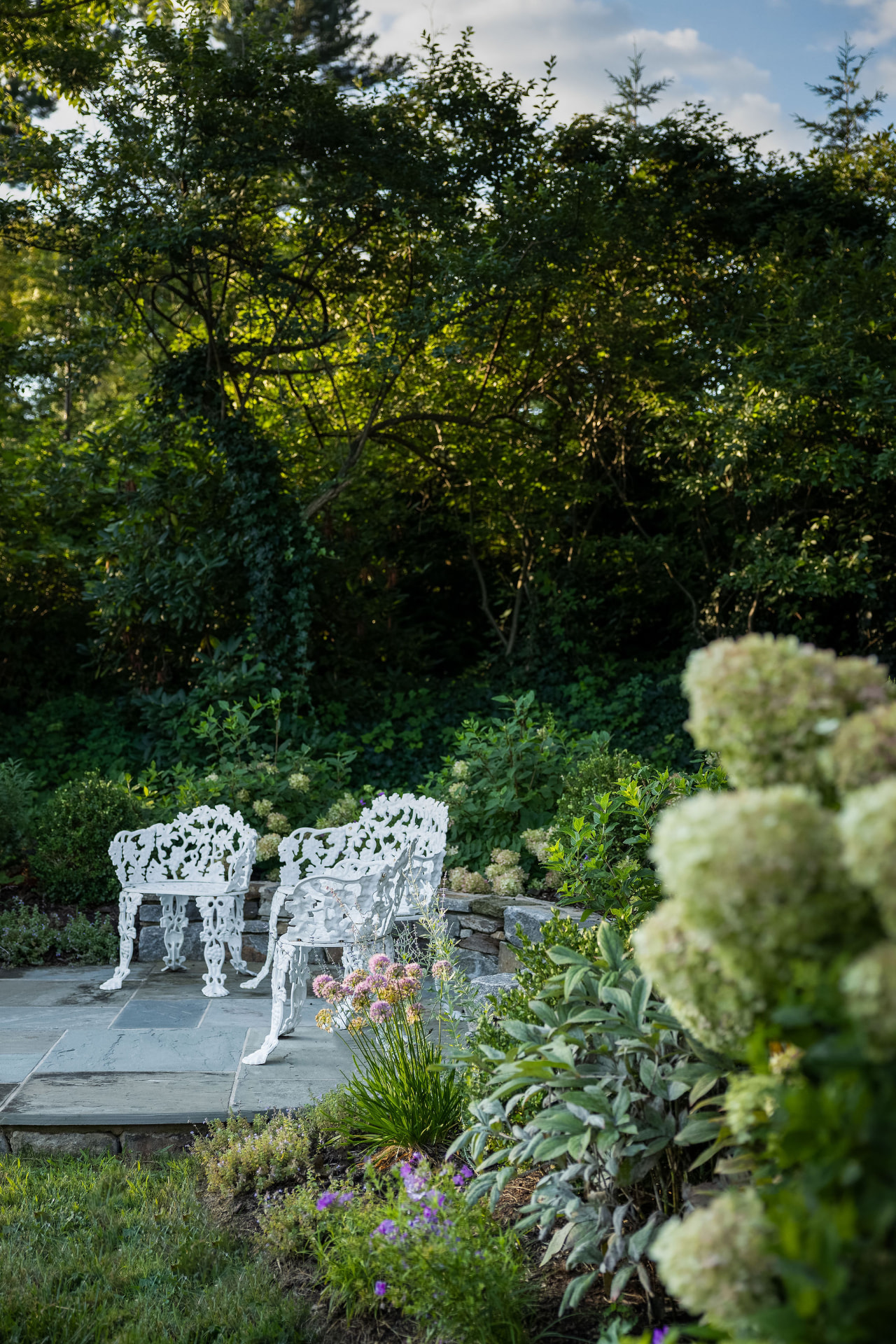 Bluestone garden patio and white seating framed by hydrangeas and perennials