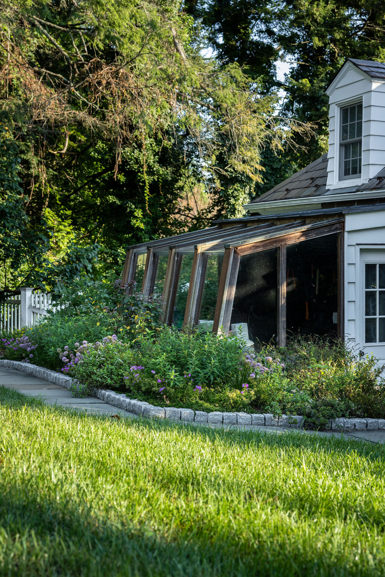 Flowering garden beds along the stone path beside an established sunroom