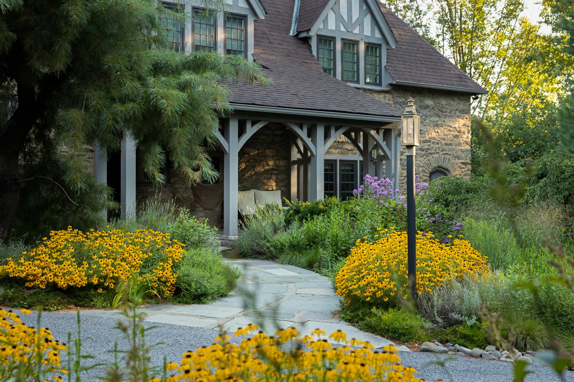 Cottage entrance with stone path, lantern, evergreens, and drifts of yellow flowers
