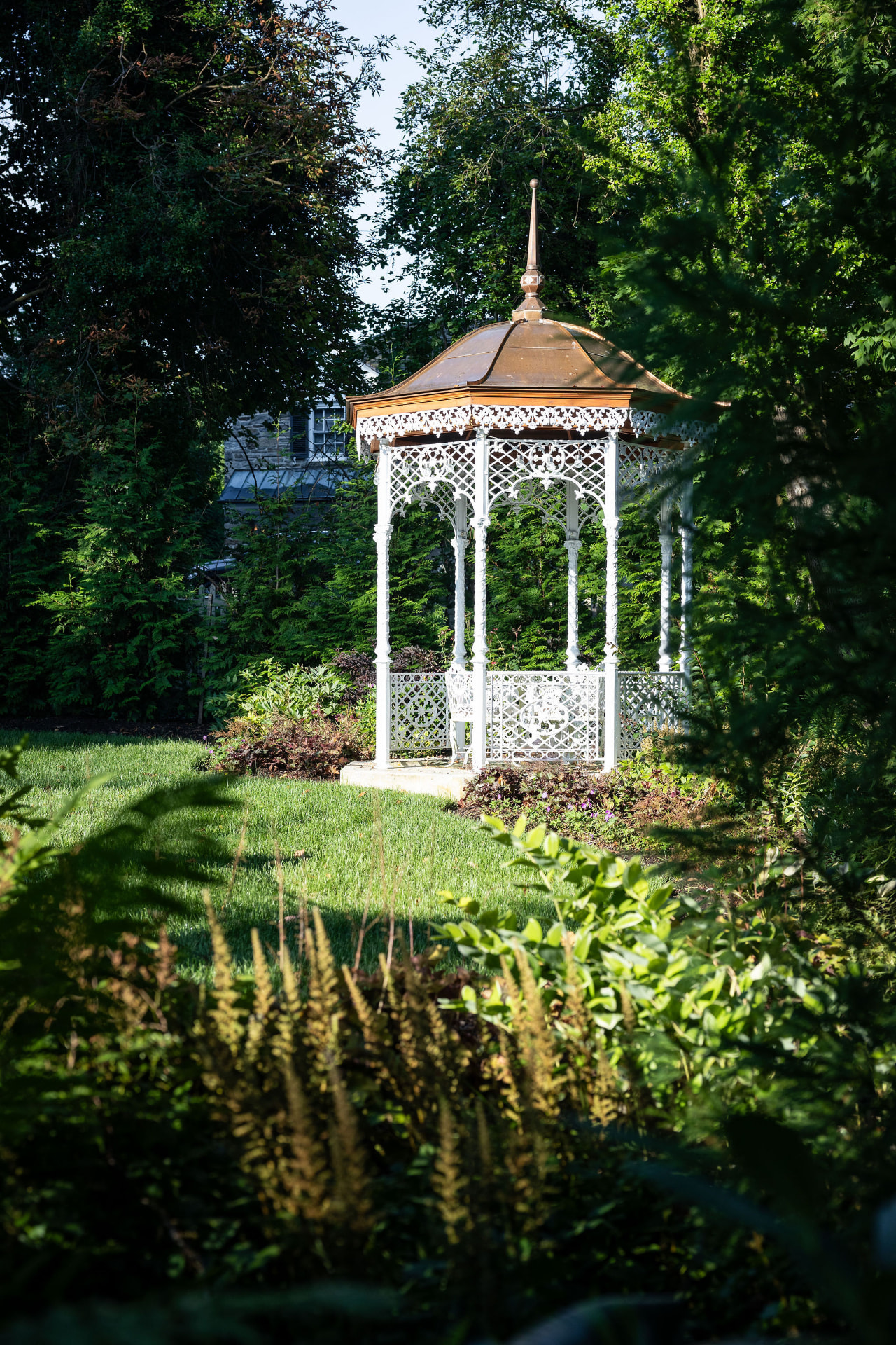 Ornate white garden gazebo surrounded by mature trees and planting