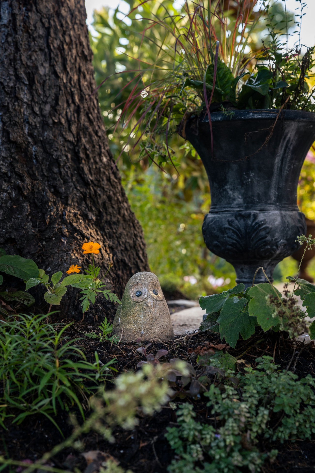 Stone owl tucked among plantings beside a black garden urn