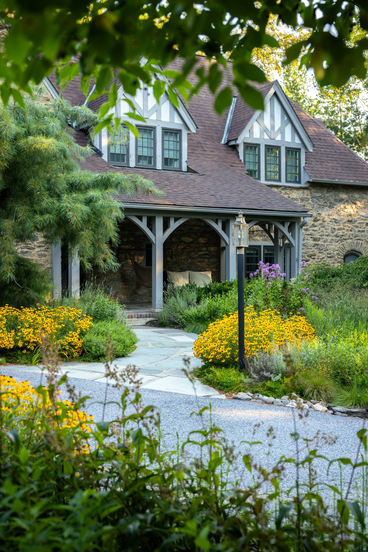 Zollinger Way cottage framed by overhanging leaves, with dormers, walkway, and summer flowers