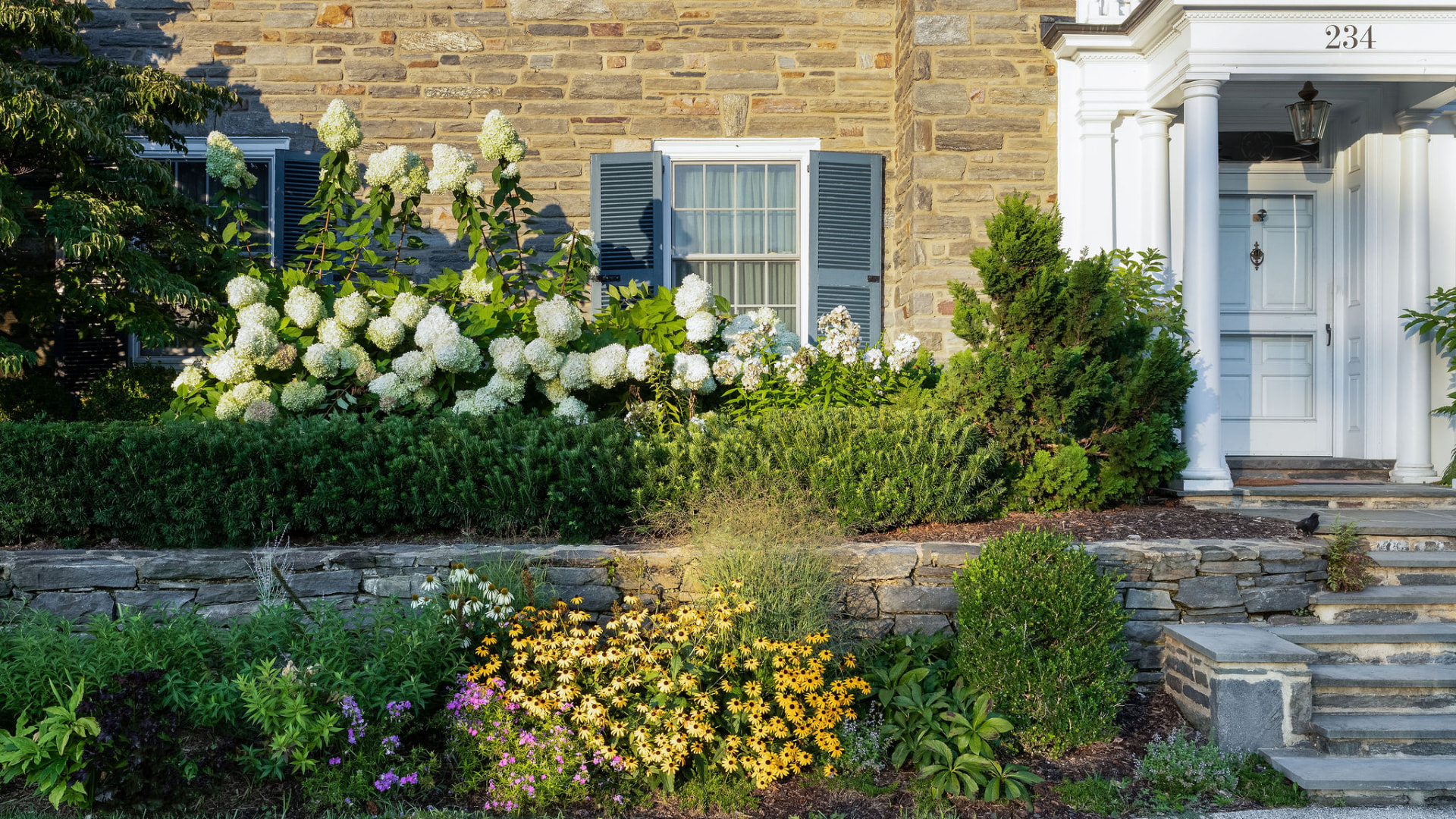 White hydrangeas and flowering perennials lining the stone entrance at Cheswold Hill