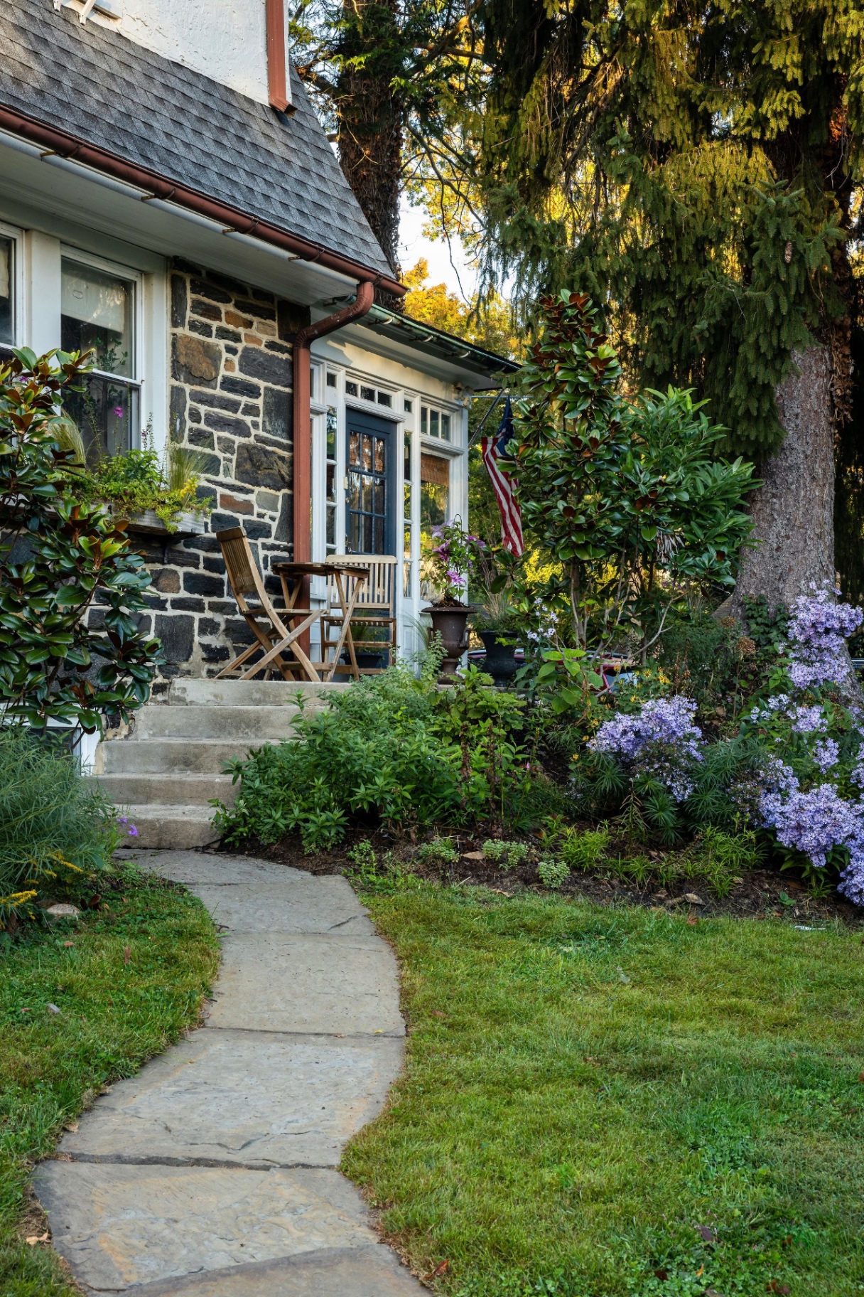 Flagstone path curving to a stone porch framed by magnolia and blue asters