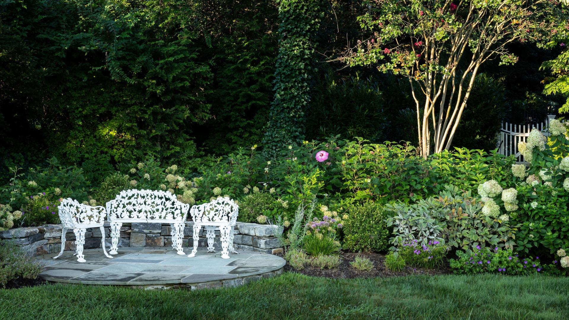 White garden seating on a circular bluestone patio surrounded by layered planting