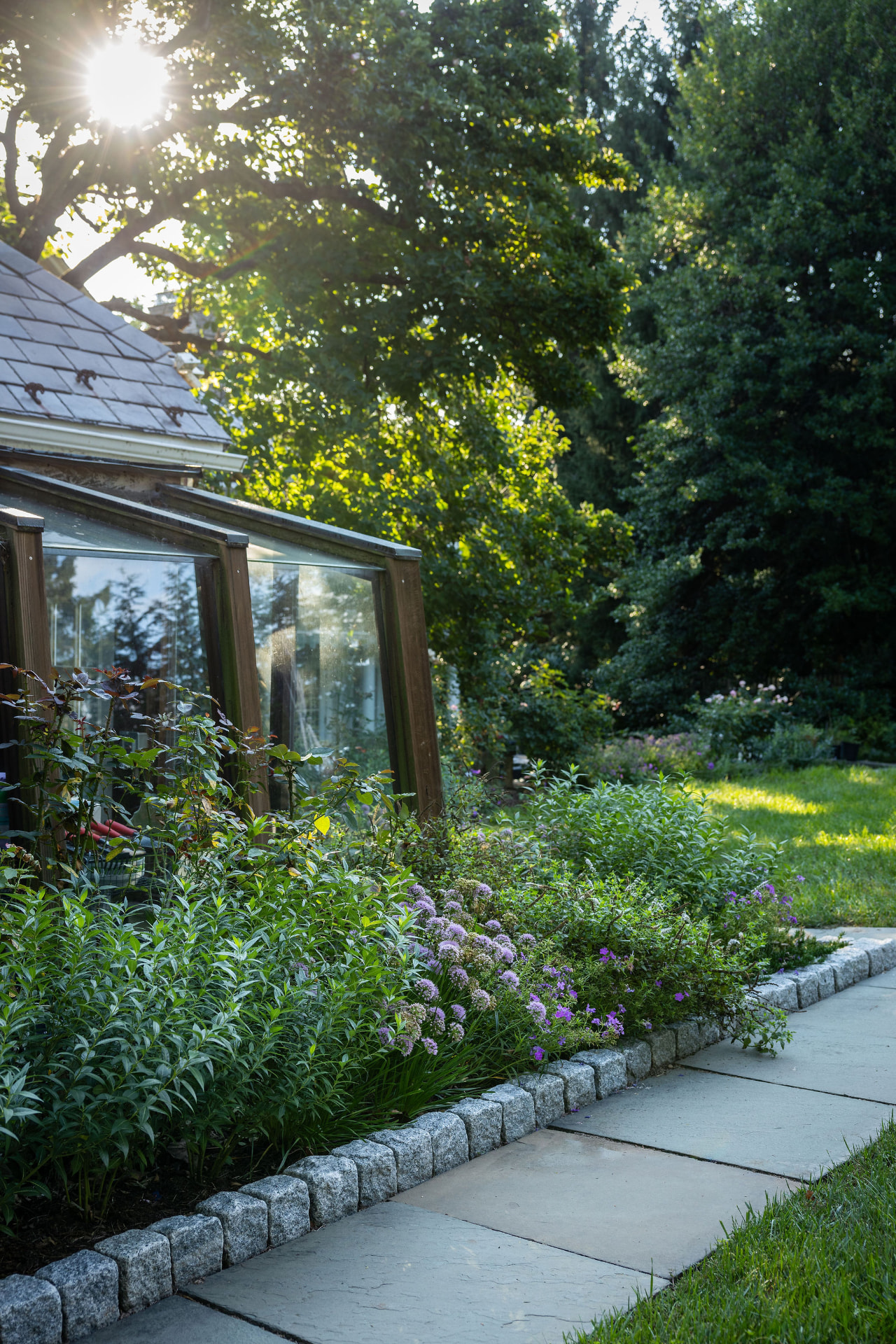 Sunlight across the garden border and stone path beside the sunroom