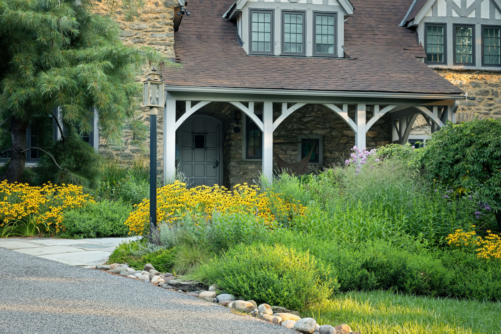 The timber-framed entry porch framed by yellow and purple flowering perennials