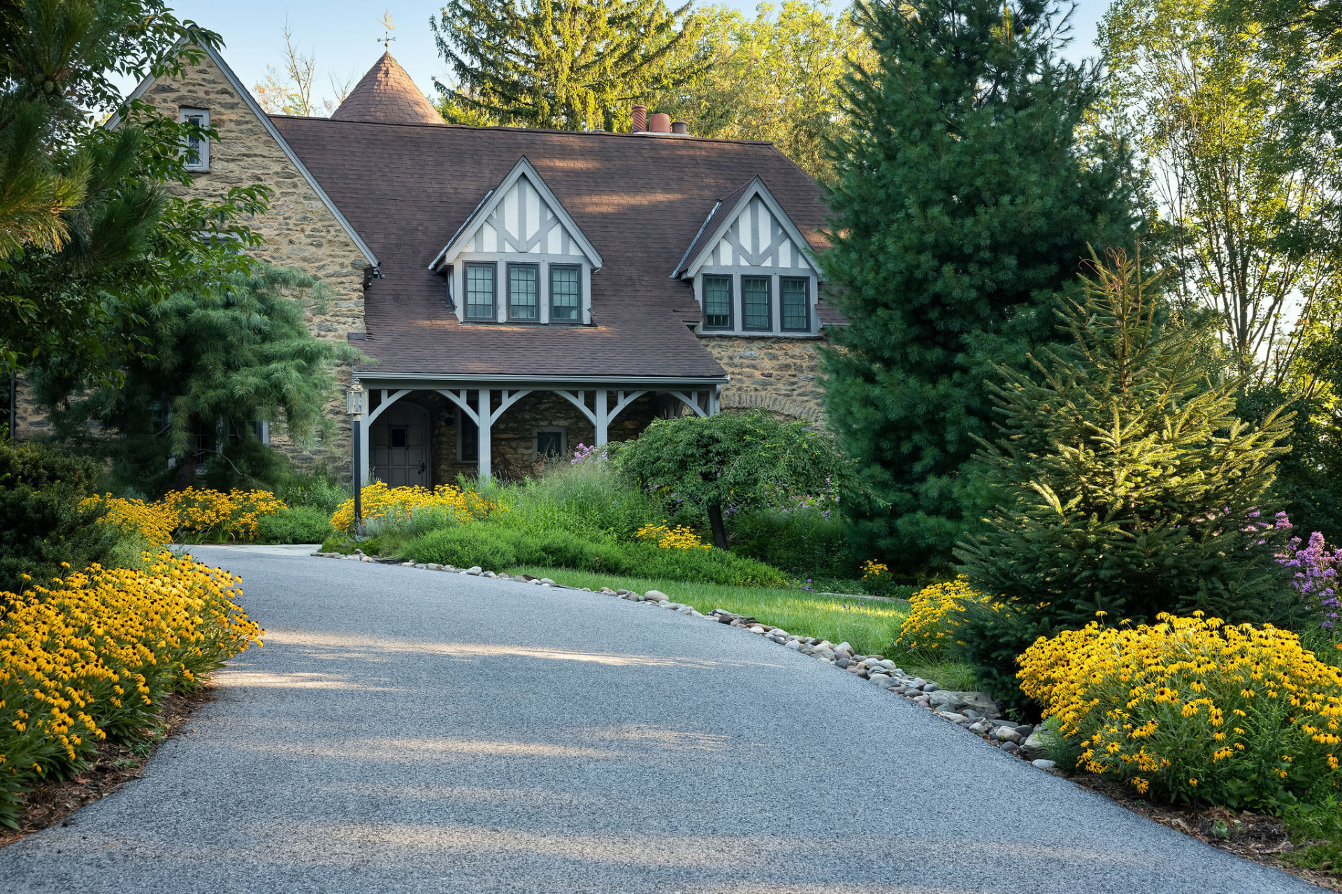 A stone and timber Tudor home on Zollinger Way with a gravel drive and layered yellow perennial planting