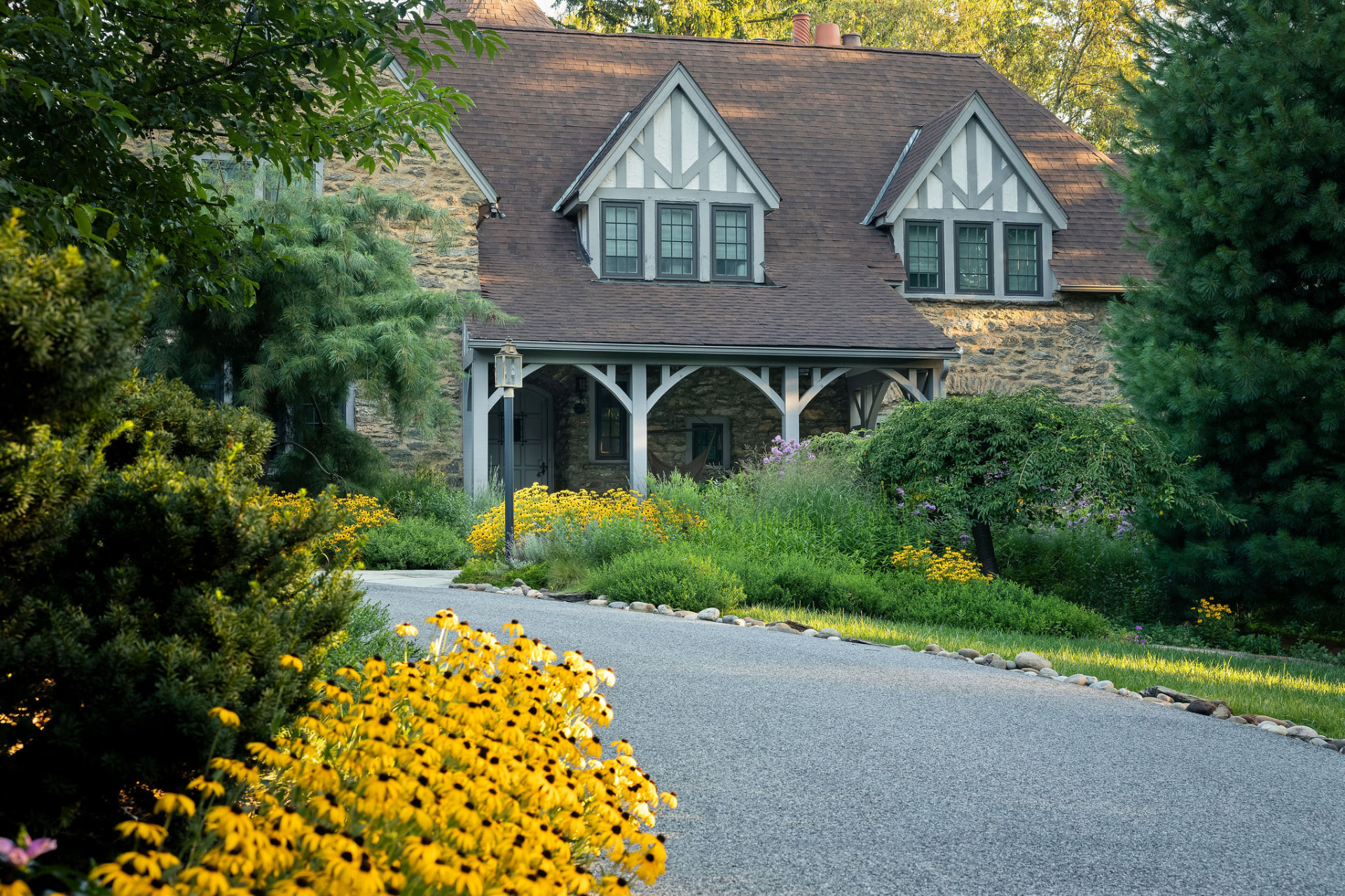 Gravel drive curving toward the stone home with layered planting on both sides