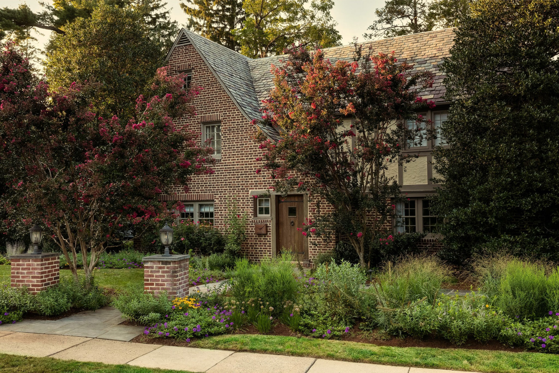Derwen Road home's brick façade and wood front door framed by crape myrtles and layered entry planting